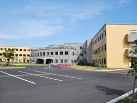 広い駐車場と、黄色い建物に挟まれているグレーの建物