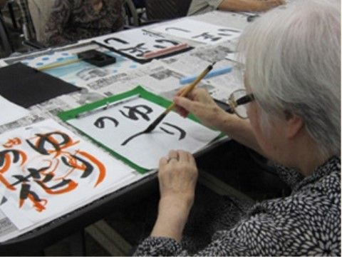 習字でゆりの花という文字を書いている白髪のおばあさん