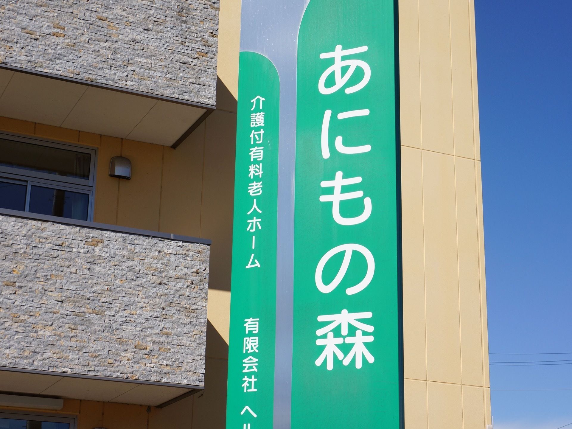 大きな文字で施設名が書かれた縦長の看板は、爽やかなグリーンと落ち着いたライトグレーが組み合わされたデザインである。
