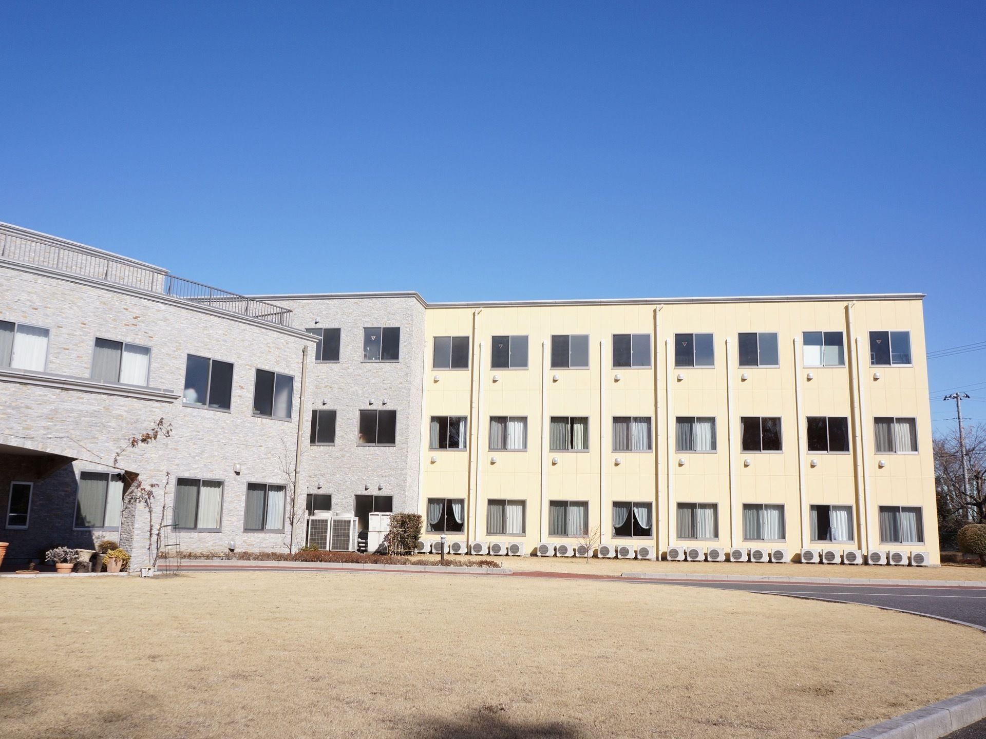 建物の右側部分はクリーム色、左側部分は淡いグレーという２色のデザインになっている。たくさんの室外機が、壁際に並んでいる。