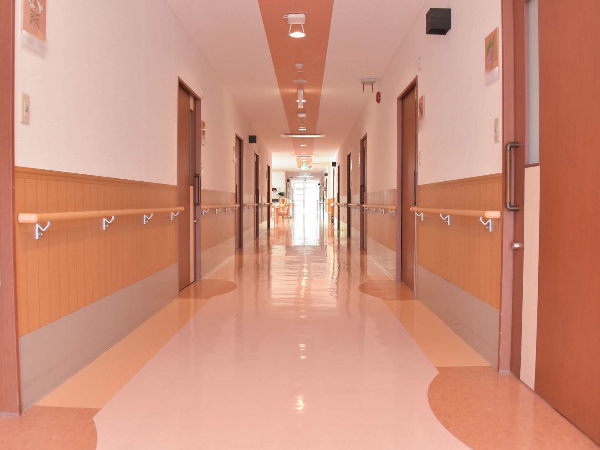 茶系統の広々とした廊下で、壁面には手すりが完備。居室のドアは引き戸で出入り口が広く車いすでもスムーズに通行できる。