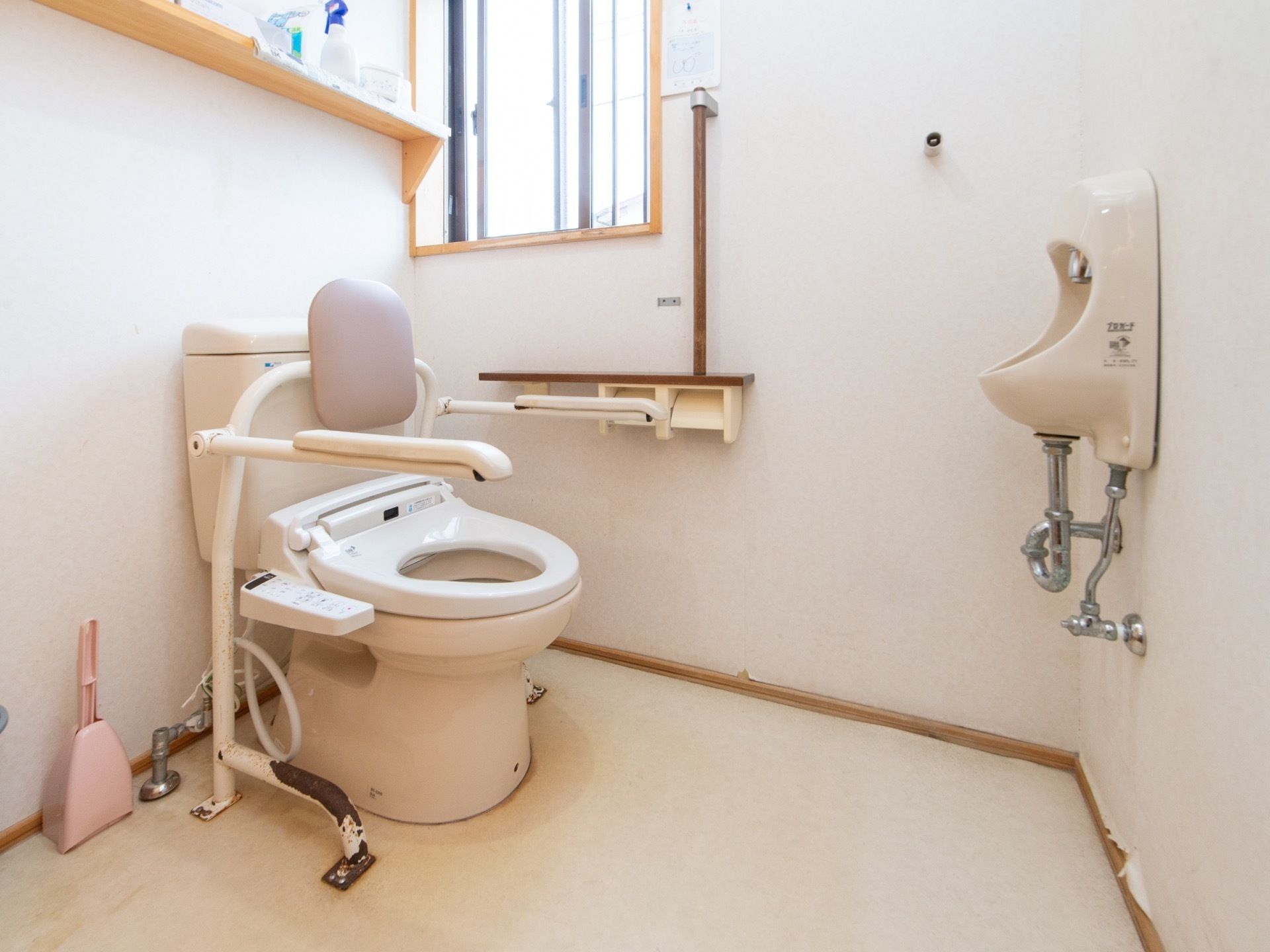 肘掛けや背もたれが取り付けられたトイレがある。便座は洗浄機付きの仕様となっている。ペーパーホルダーの上部には手すりがついている。