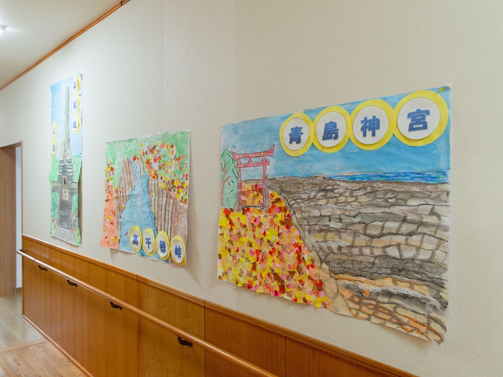 壁面に入居者様が描いた近隣の観光スポットなどの絵が展示されている。その下には手すりが取り付けられている。