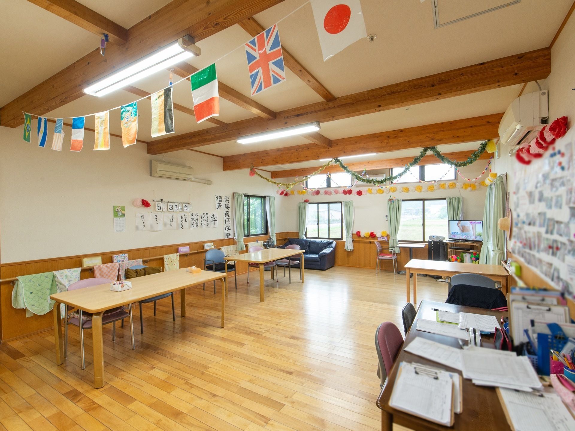 入居者様が使用するテーブルやソファが置かれている。壁面にはエアコンが数台設置されているほか、写真なども飾られている。