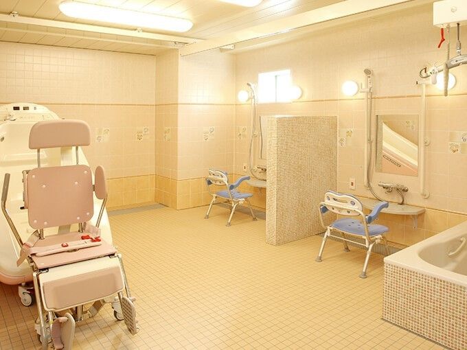 施設内のバスルームには洗い場が広く設けられている。椅子が置かれている。床はタイル張りになっている。バリアフリーの機械もある。