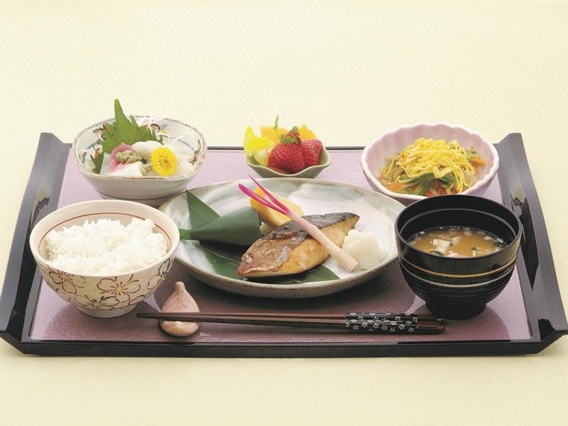 黒とピンクのトレイに配膳された、焼き魚や小鉢などの食事