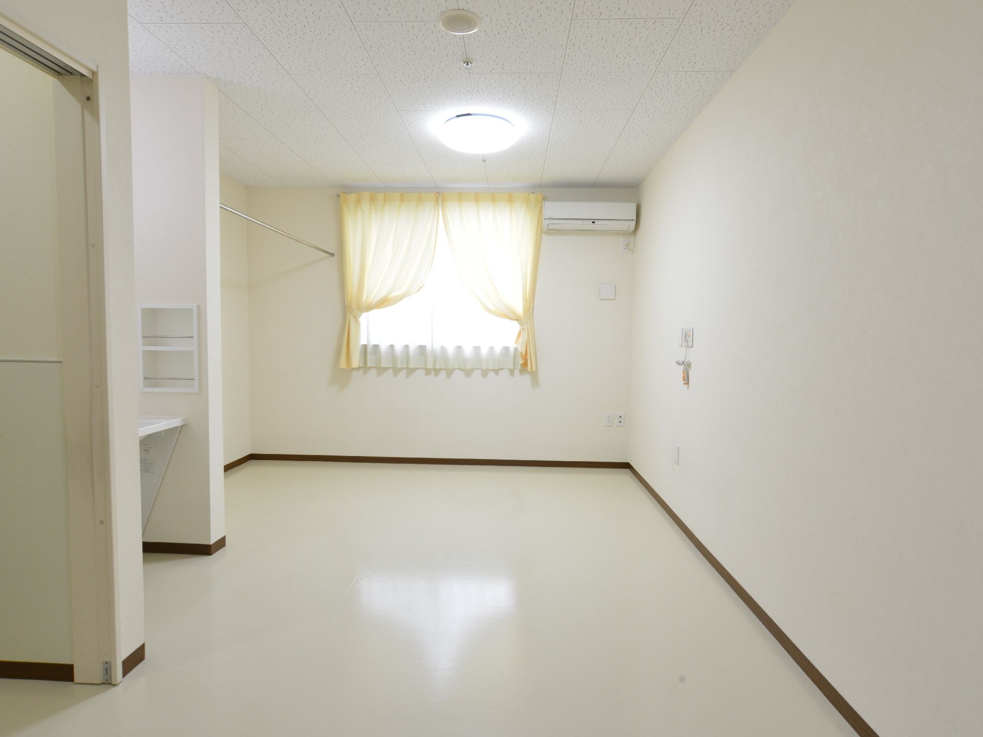 壁や床を白で統一し、黄色いカーテンがアクセントになっている居室