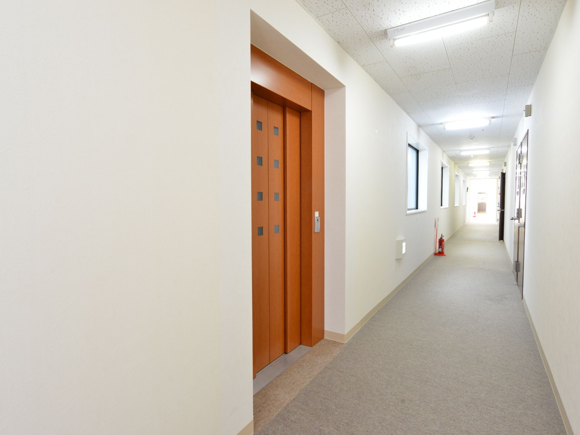 明るい茶色の扉のエレベーター。大きな形のものではないせいか、普通の住宅と変わりない印象を受ける。白をベースにしているので、清潔な印象。