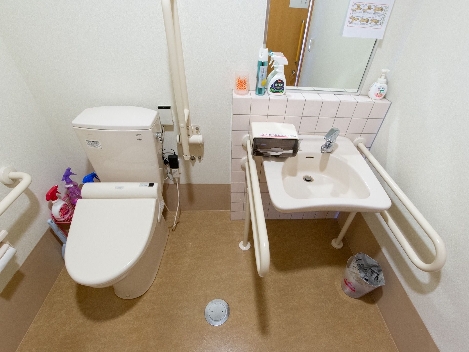 広々とした清潔感のあるトイレである。温水洗浄便座やペーパータオルの備わった洗面スペース、手すりが完備されている。