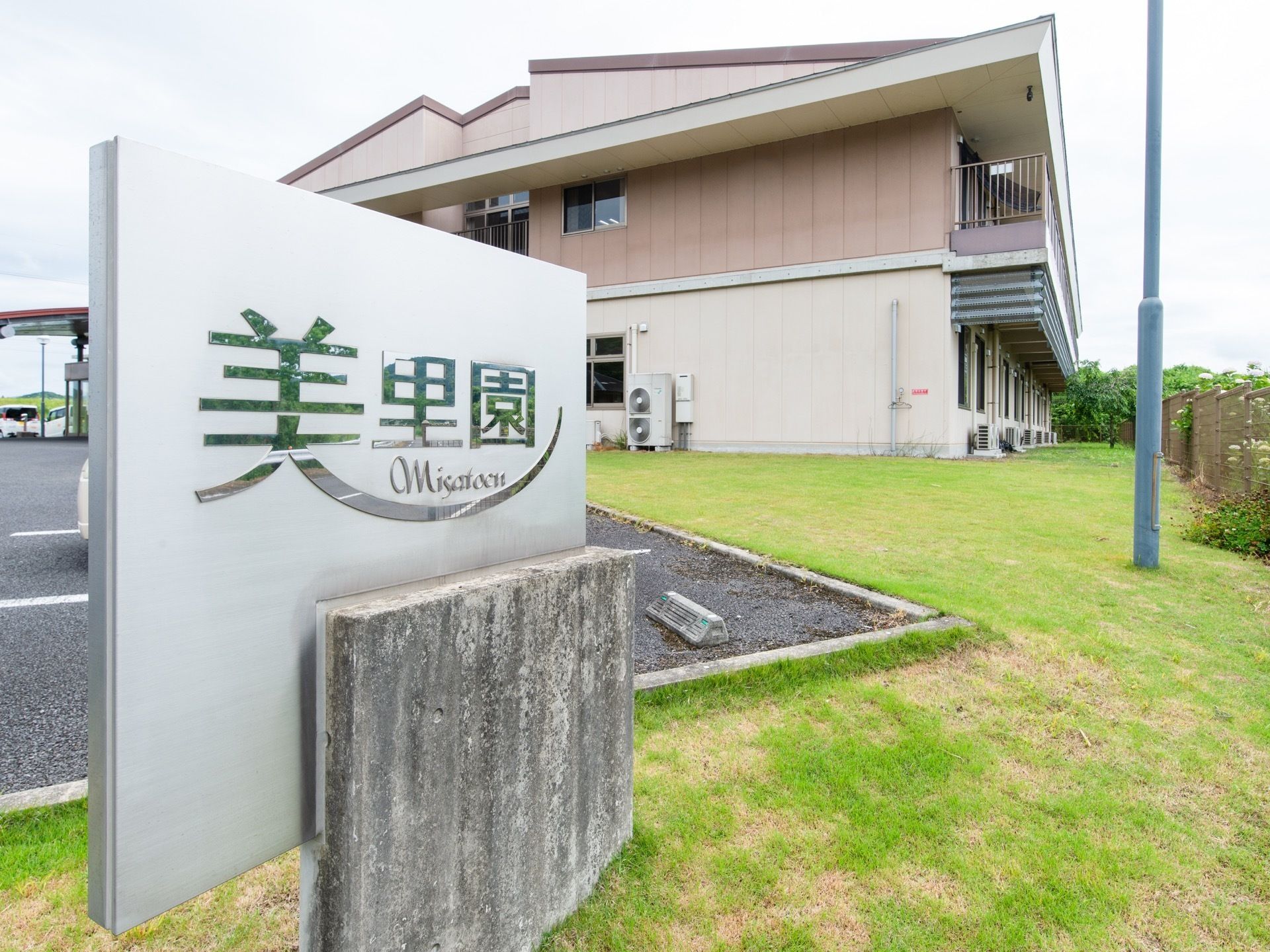 施設の入口に施設名の書かれた看板が建てられている。周辺は芝生が広がりグリーンが美しい。横に駐車スペースがある。