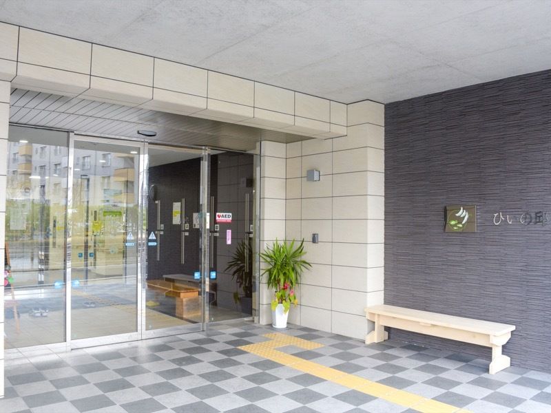 エントランスの壁には施設名が書かれた看板を設置している。また入り口にはインターホンがあり、腰掛けるためのベンチが置かれている。