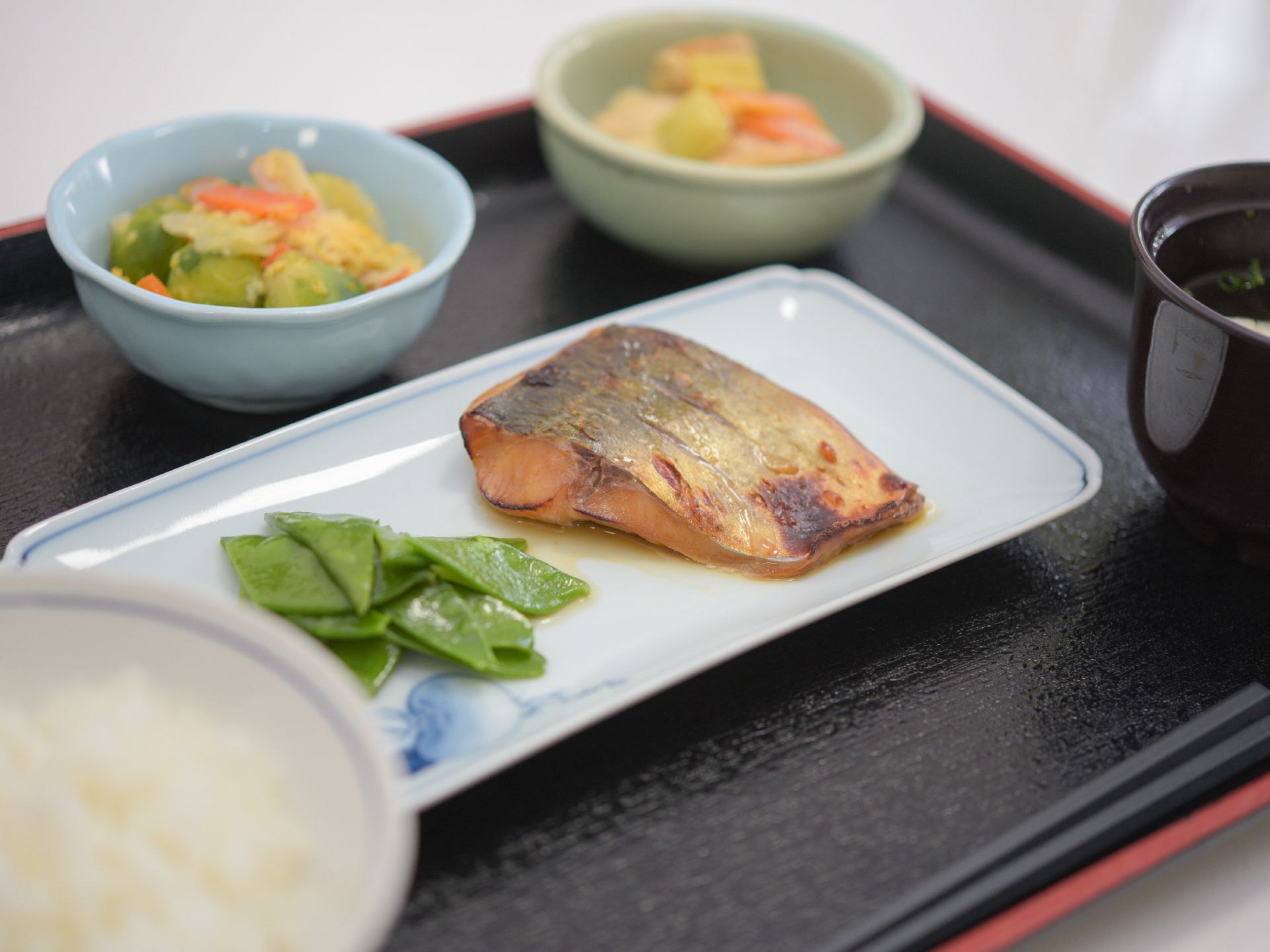 黒いトレイに盛りつけられている、焼き魚、２つの小鉢などの食事