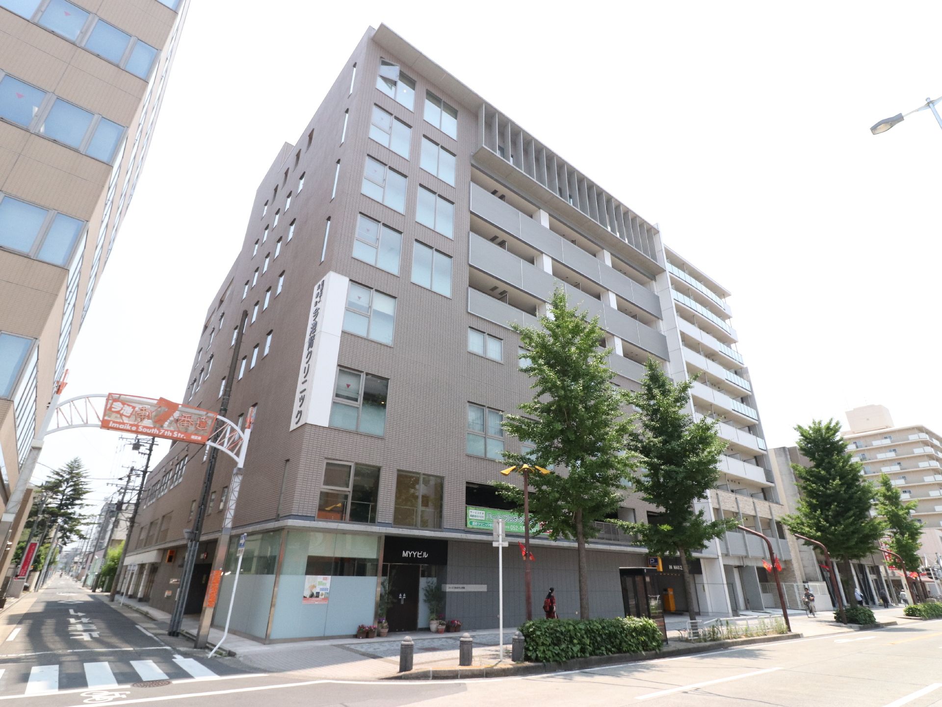 3、4階部分にクリニックの看板がある。外壁はブラウン系。建物は道路に面している。近隣はビルが立ち並んでいる。