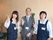 笑顔でピースサインをしているスタッフ。女性は紺色のエプロンを着用、男性はグレーのスーツ。名札を付けている。