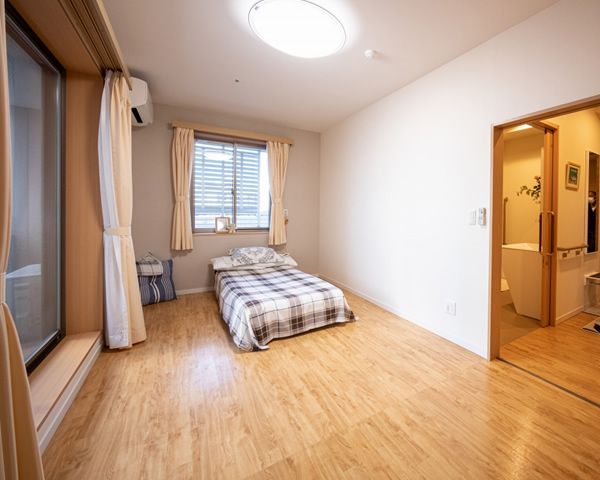 窓が大きく明るい室内。ベランダがある。窓際には、高さの低いベッドが2つ置かれている。壁にはナースコールがある。