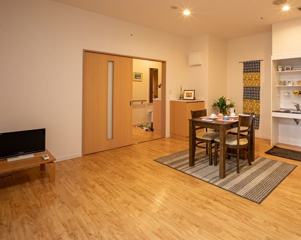 部屋は広々としている。扉は大きく引戸タイプ。部屋には木製のテーブルと椅子、窓際にはソファーと観葉植物が置かれている。