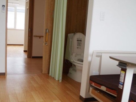 居室にはトイレが完備されており、扉は開閉がしやすいアコーディオンカーテンになっている。介護ベッドが壁際に置かれている。