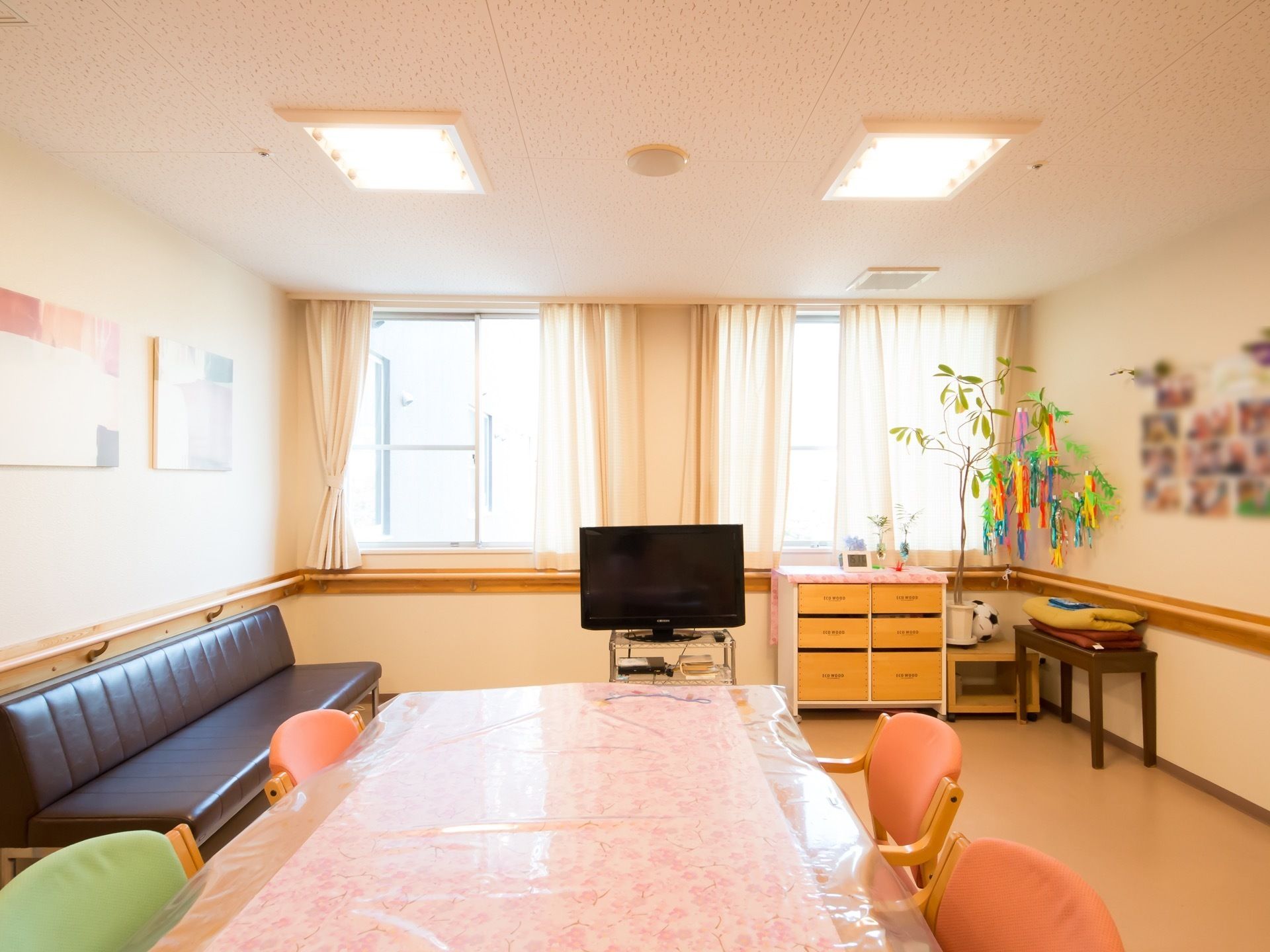 壁には手すりが付けられ、窓にカーテンがかかっている。室内にはイスやテーブル・テレビなどが置かれ、季節行事の飾りや写真などが貼られている。