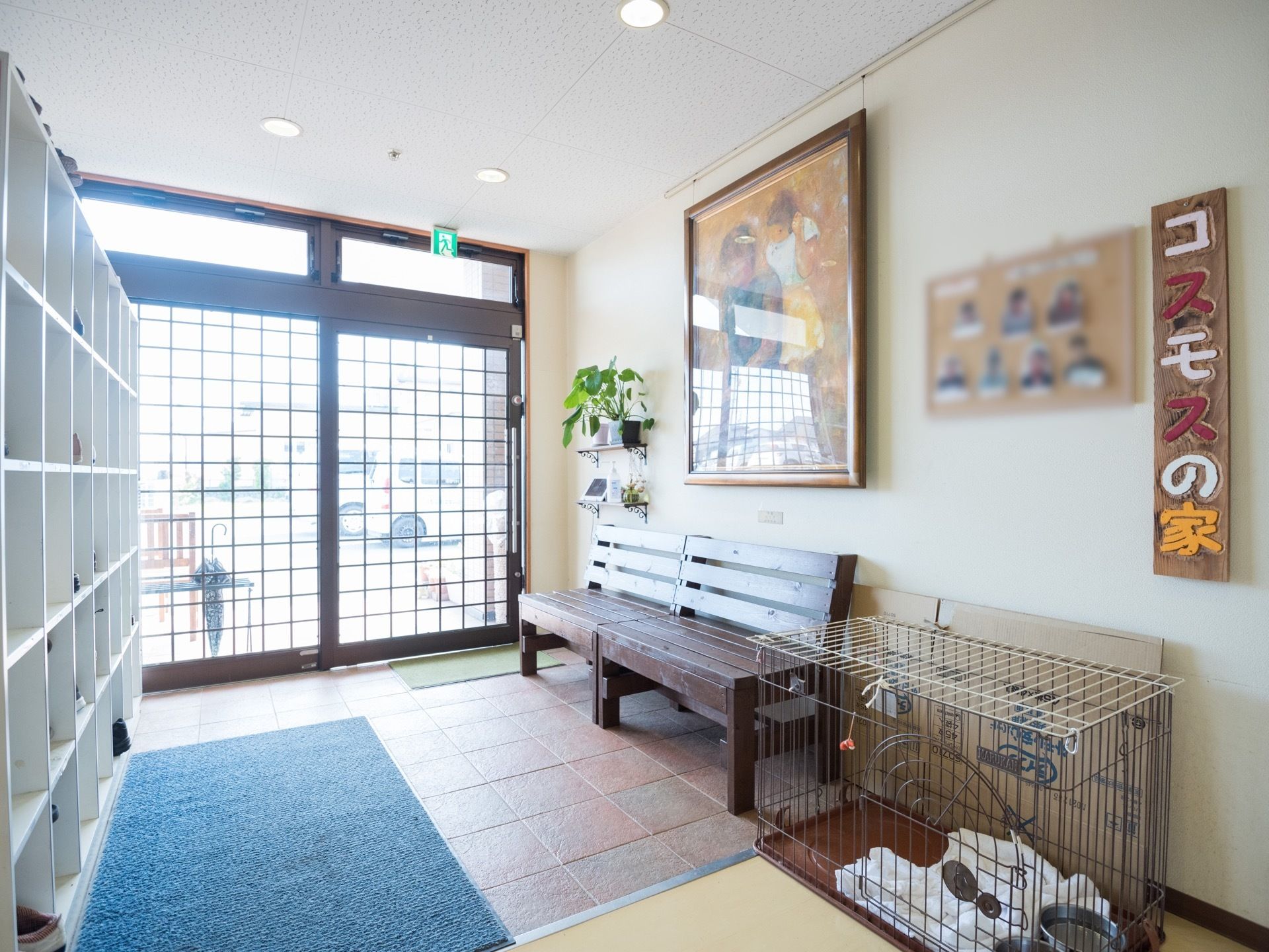 格子のガラス扉の玄関である。中には、ベンチが並べて置かれており、その上の壁には大きな絵が飾られている。