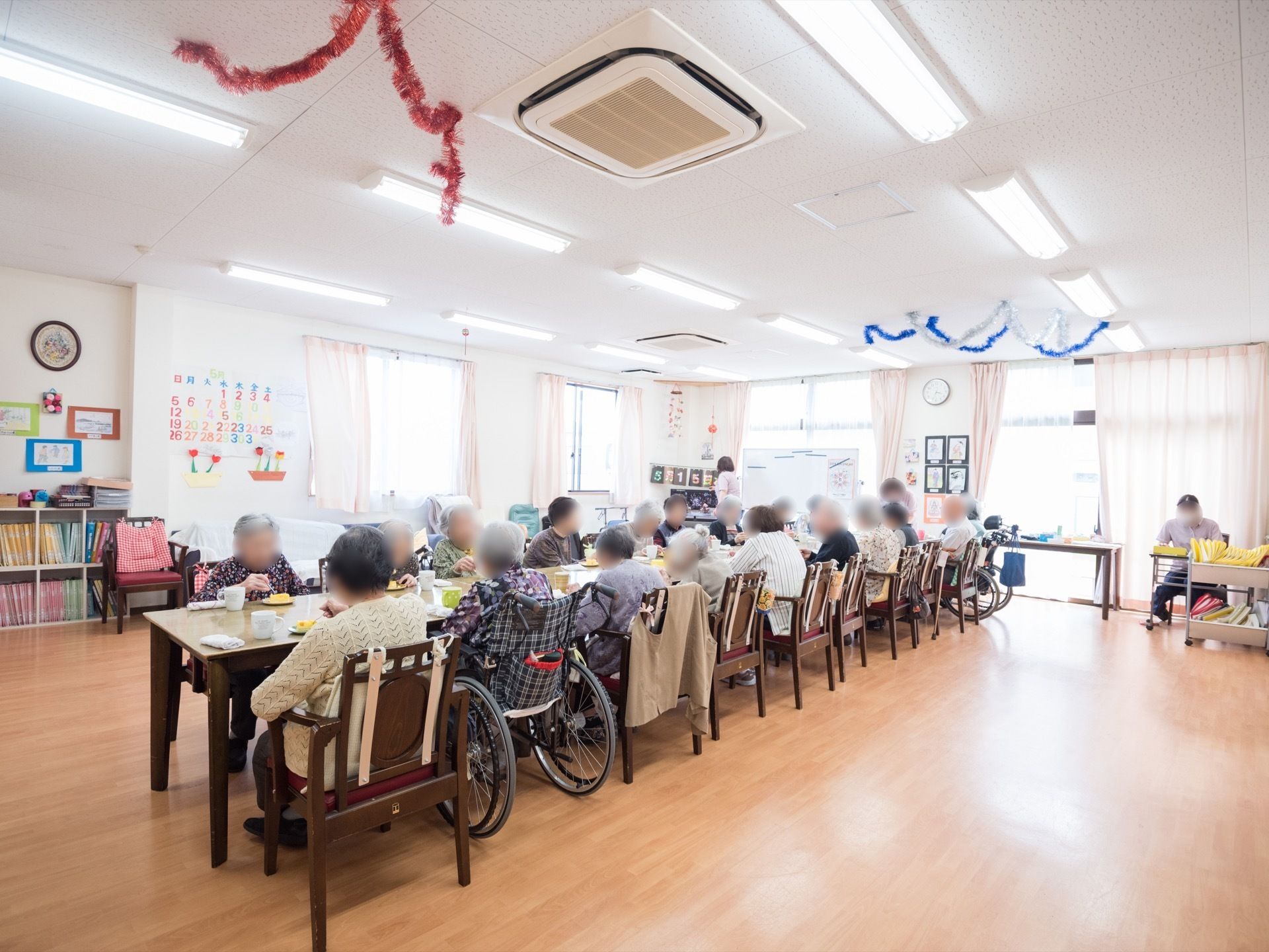 明るく開放的な食堂。中央にダイニングテーブルが設置されており、入居者様が集まっておやつタイムを楽しんでいる。