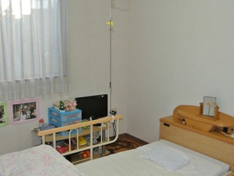 リハビリ用ベッドには、時計などの小物を置くスペースがある。壁にはレクリエーションの写真などが貼られている。