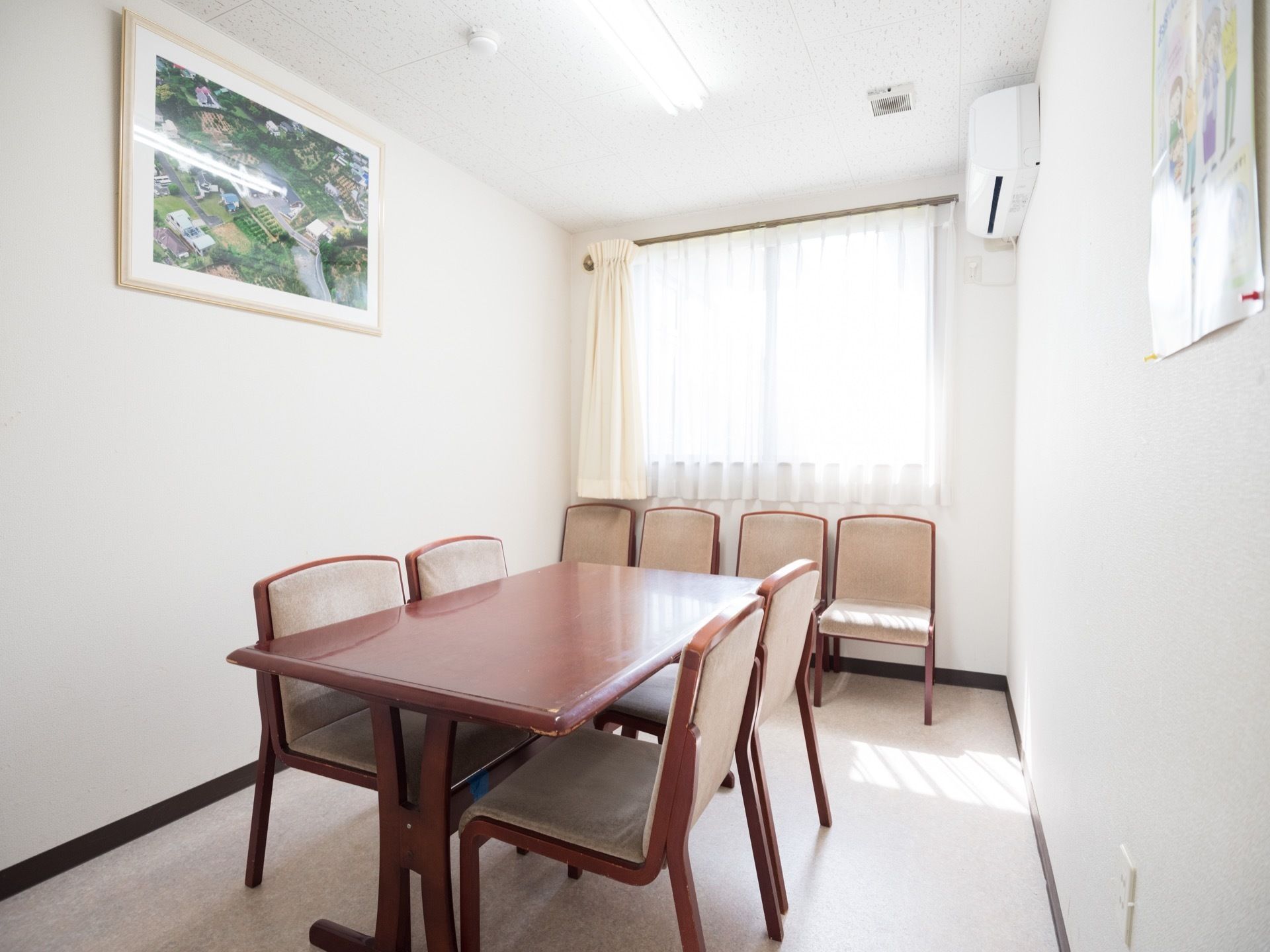 室内は白色を基調とした明るい雰囲気で、外光も差し込んでいる。テーブルと椅子が置かれ、壁には施設の航空写真が飾られている。