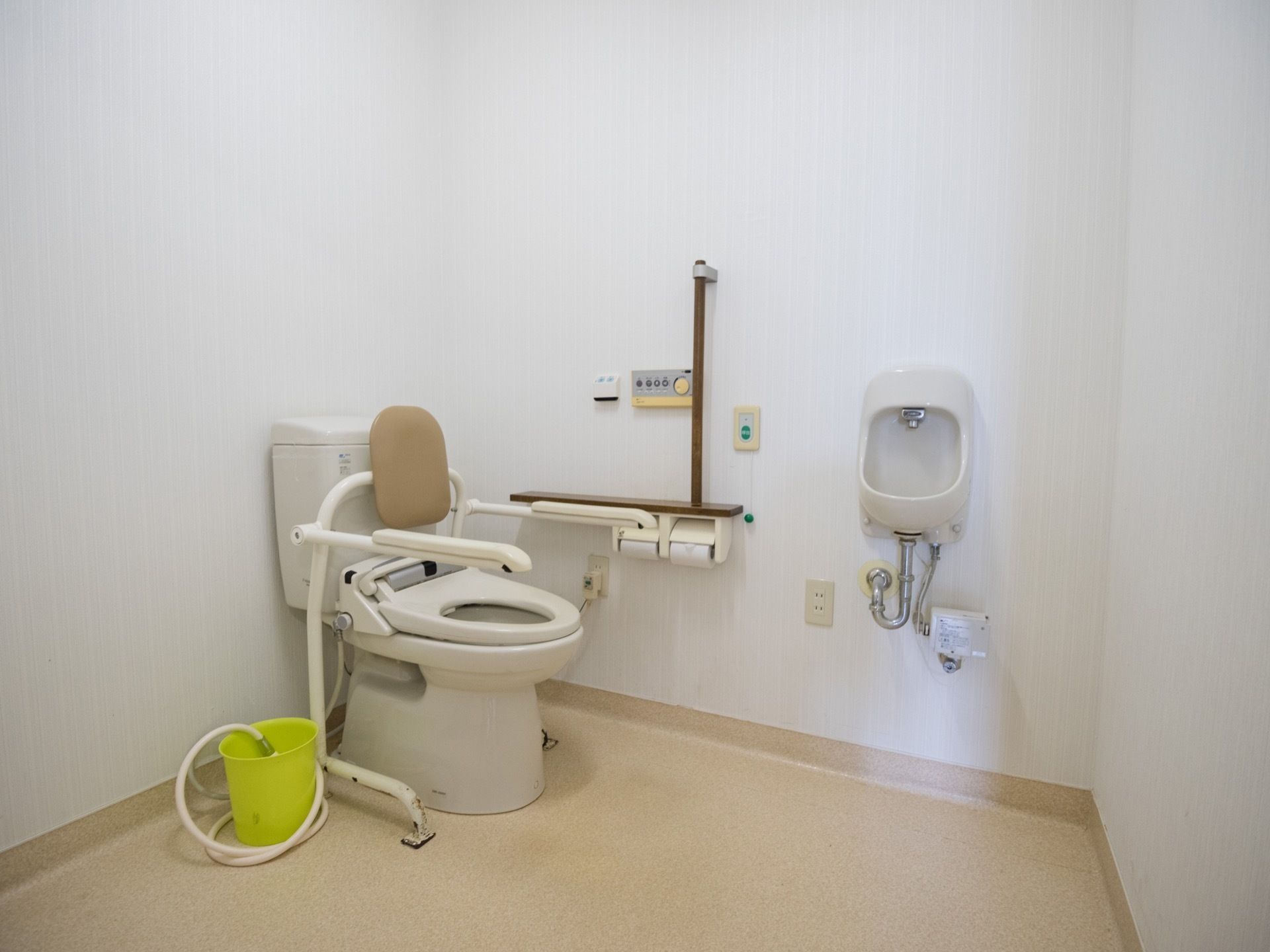 温水洗浄便座仕様のトイレで、両脇に肘掛け、後ろには背もたれがついている。また、壁にあるボタンで操作が可能となっている。