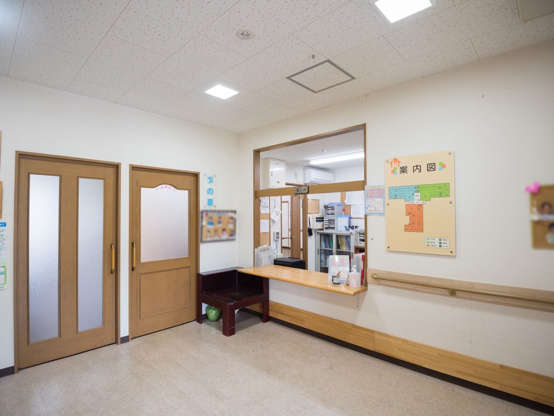 白色を基調としたフロアに、面会室や共有スペースの出入口、受付がみられる。角には椅子が置かれ、壁には案内図が表示されている。