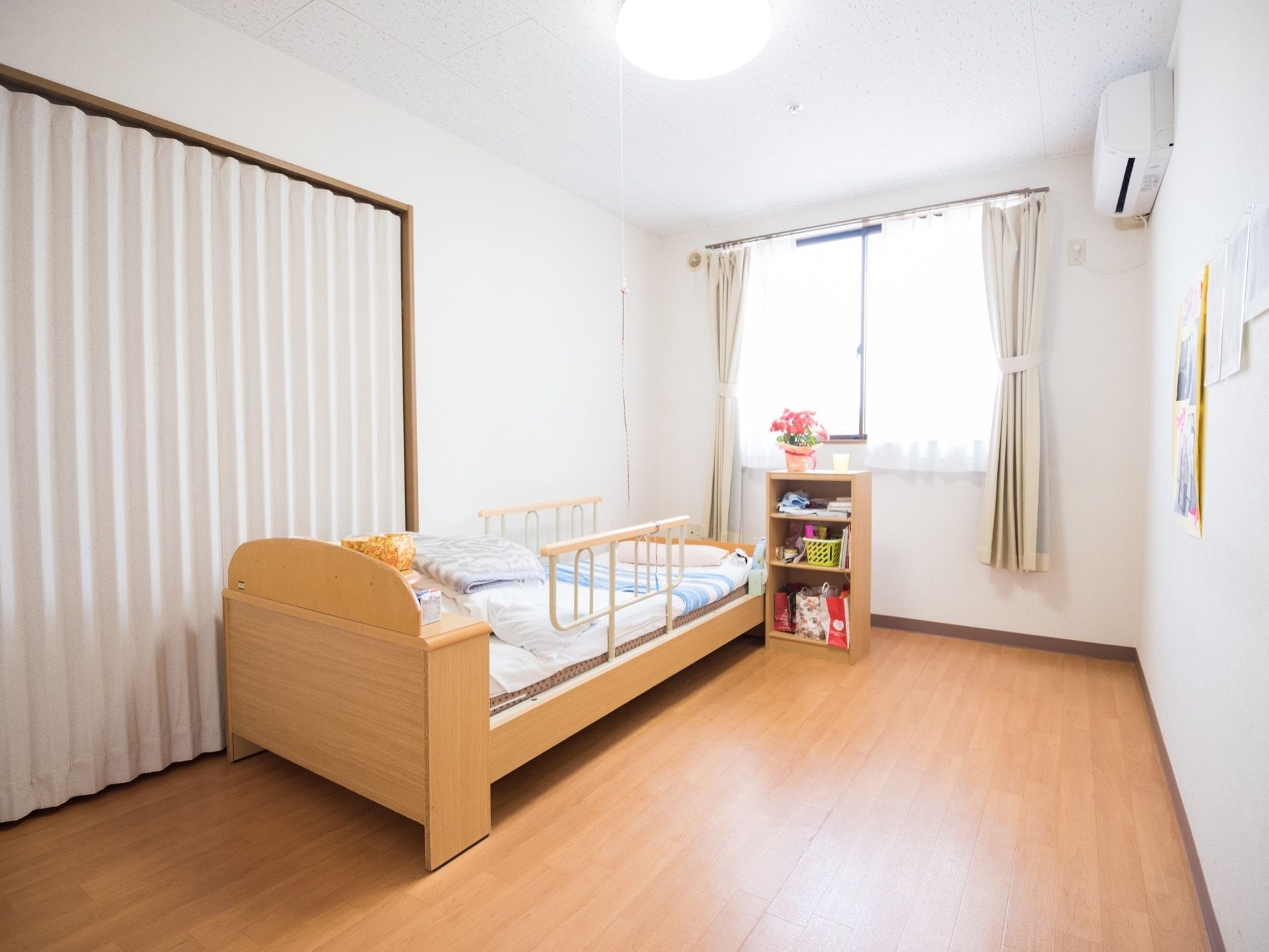 白色を基調とした居室はとても明るい雰囲気である。介護用ベッドに戸棚、エアコンなどが設置されている。日当たりも良い。