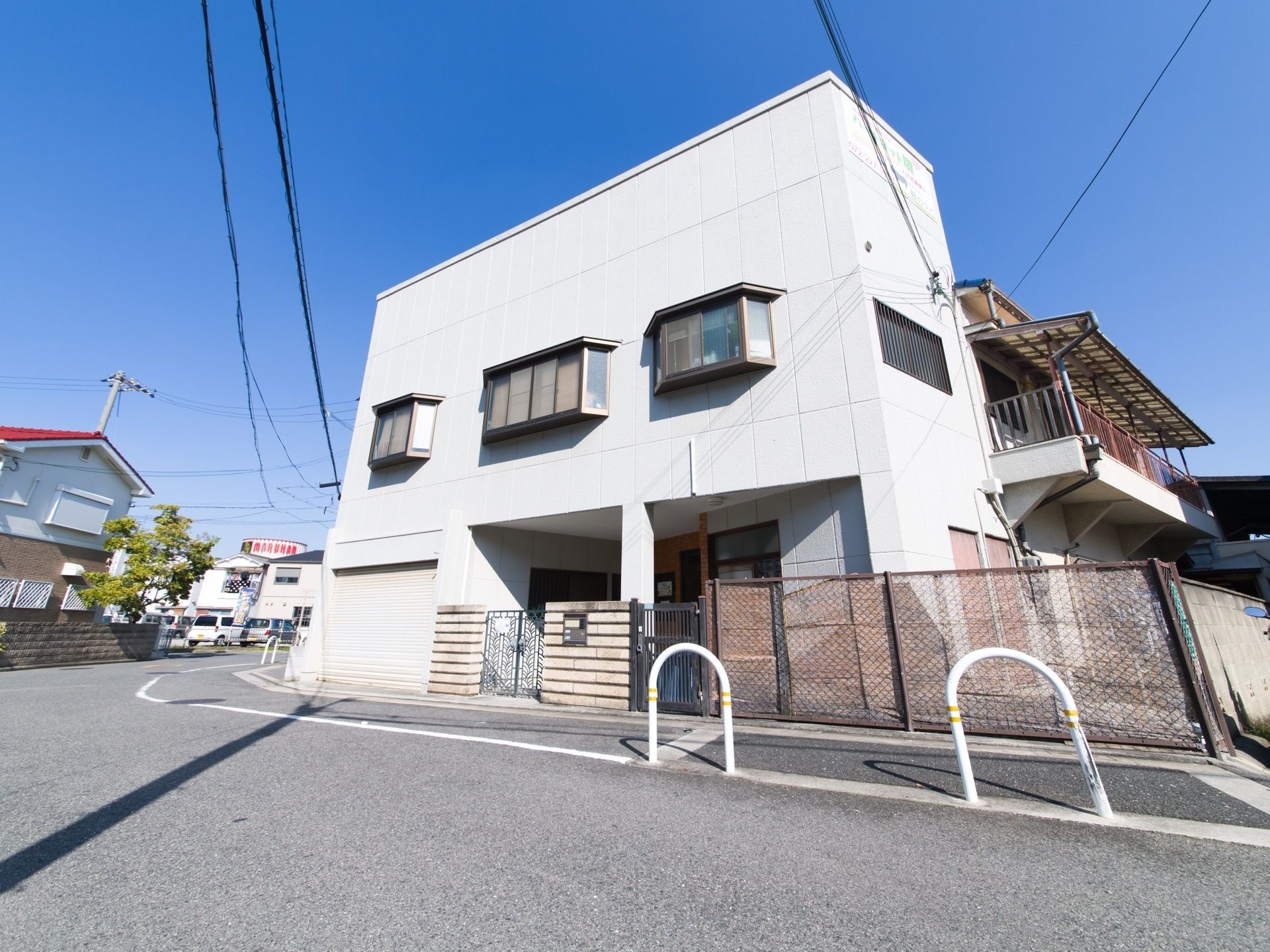 アーチ状の柵が立つ通りに面している、２階建ての白い建物
