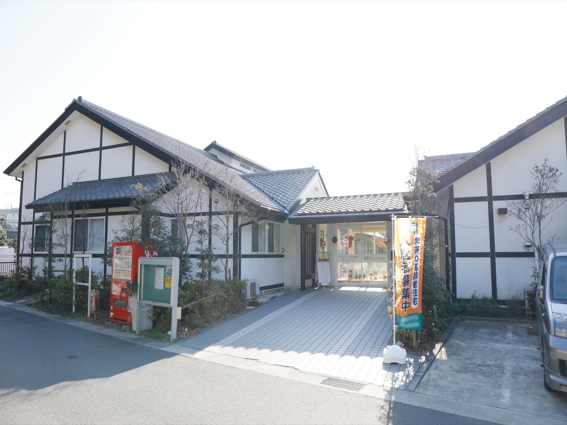 施設の建物は白と黒を基調としたもので、屋根には瓦が用いられている。施設前には自動販売機が設置されている。