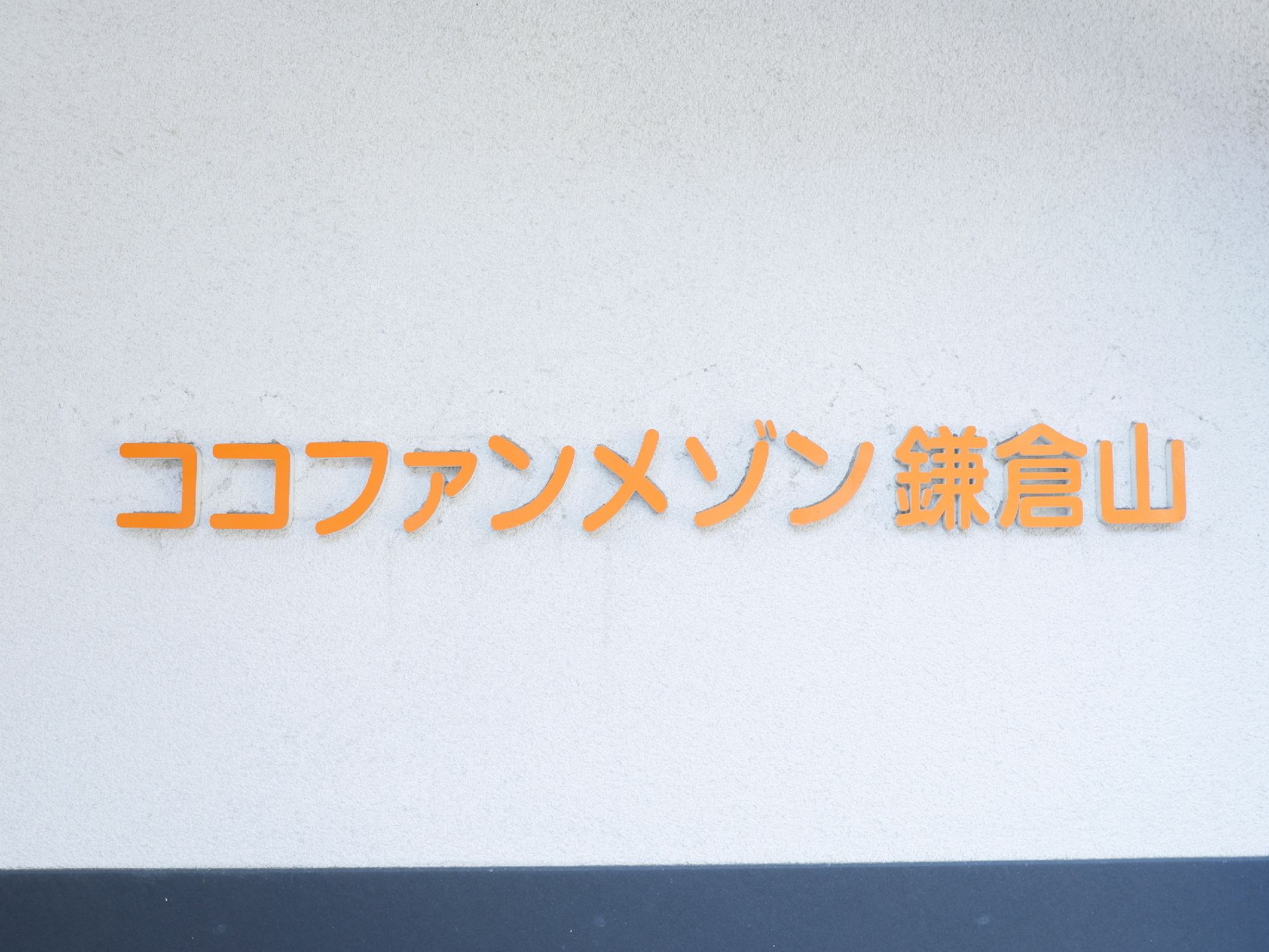白い壁に、オレンジ色で大きく読みやすい文字で書かれた施設の看板