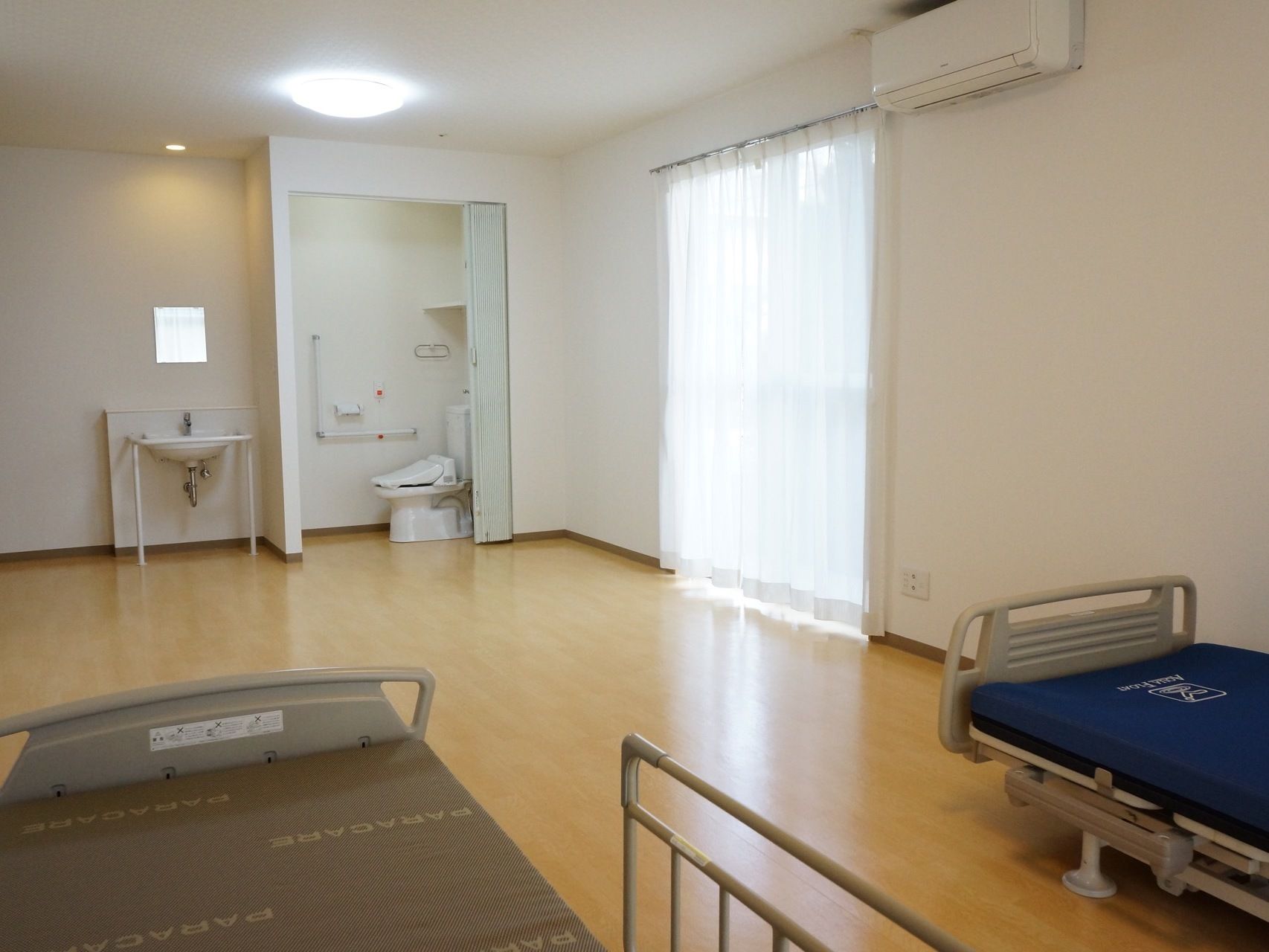 夫婦共用の居室には、洋式トイレ、洗面台、介護用ベッド、エアコンが設けられている。掃き出し窓からベランダに出ることができる。