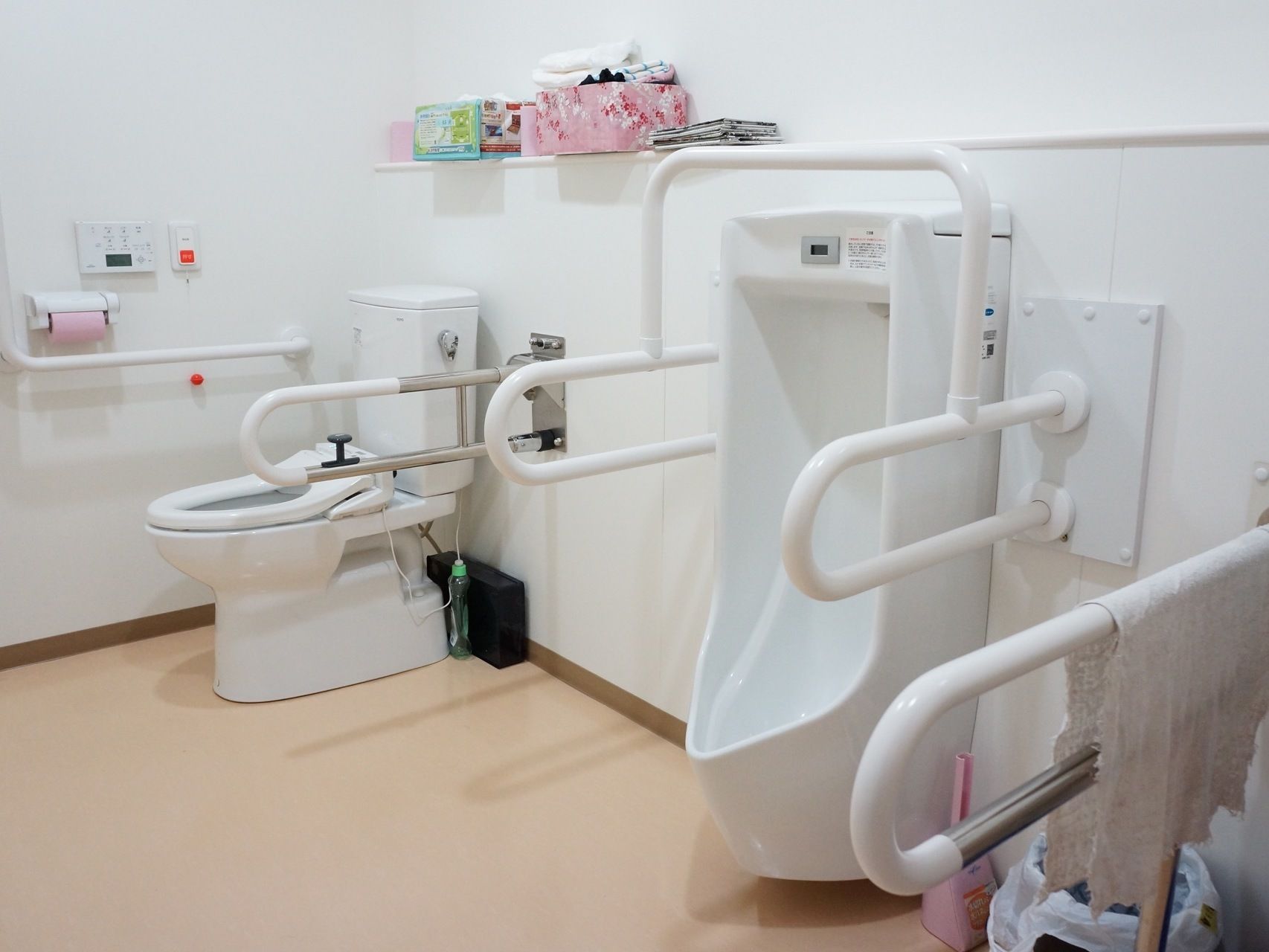 男女兼用の便座と、男性用の便器が隣り合って設置されている。どちらにも周囲に手すりがついている。掃除用具もある。