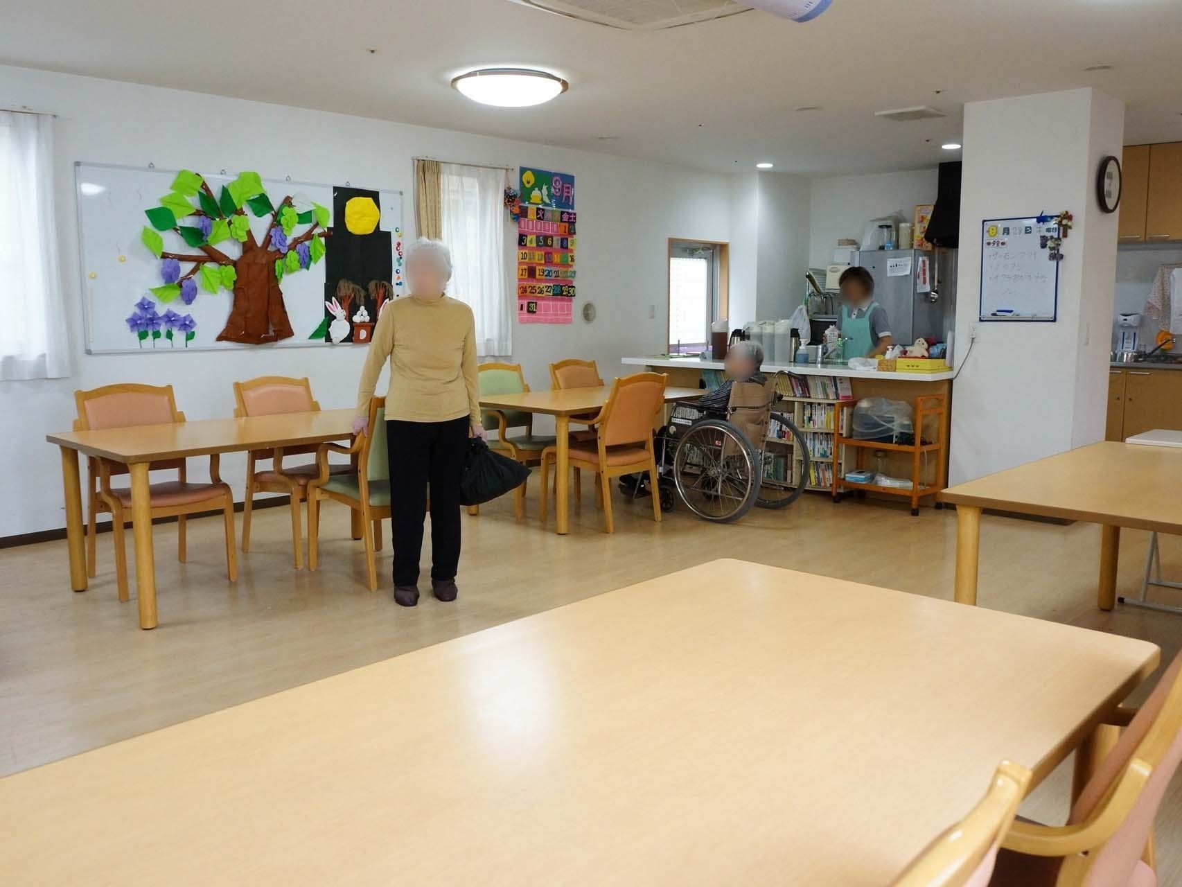 共有スペースの壁には、月やウサギ、木々といった紙工作が貼られており、入居者様の目を楽しませている。2人の入居者様と1人のスタッフがいる。