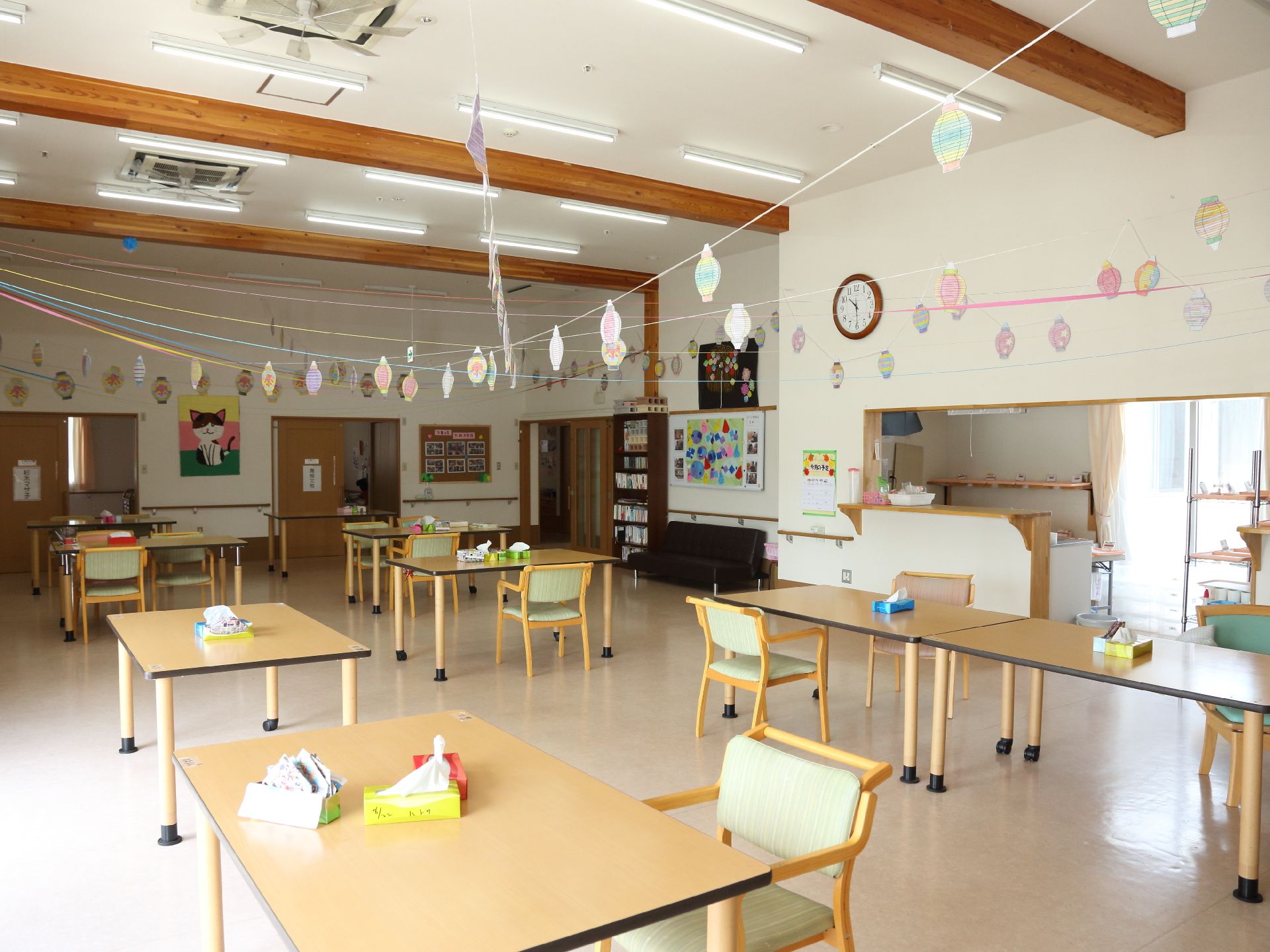 広々とした食堂。机と椅子が複数配置されている。天井と壁には手作りの飾りがあり、壁には手摺が設置されている。