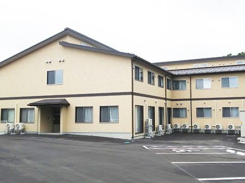 2階建てで黄色味を帯びた外壁の施設である。玄関口には黒い屋根が取り付けられている。駐車スペースには車椅子専用の場所も用意されている。