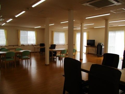 蛍光灯がたくさんつけられている部屋にはテーブル、椅子も複数用意されている。窓にはレースと黄色いカーテンがかけられている。