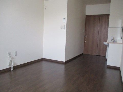 白色の壁紙、ダークブラウンの落ち着いたフローリングの部屋には洗面台が設置されている。壁にはタオルハンガーがある。近くには茶色い扉がみえる。