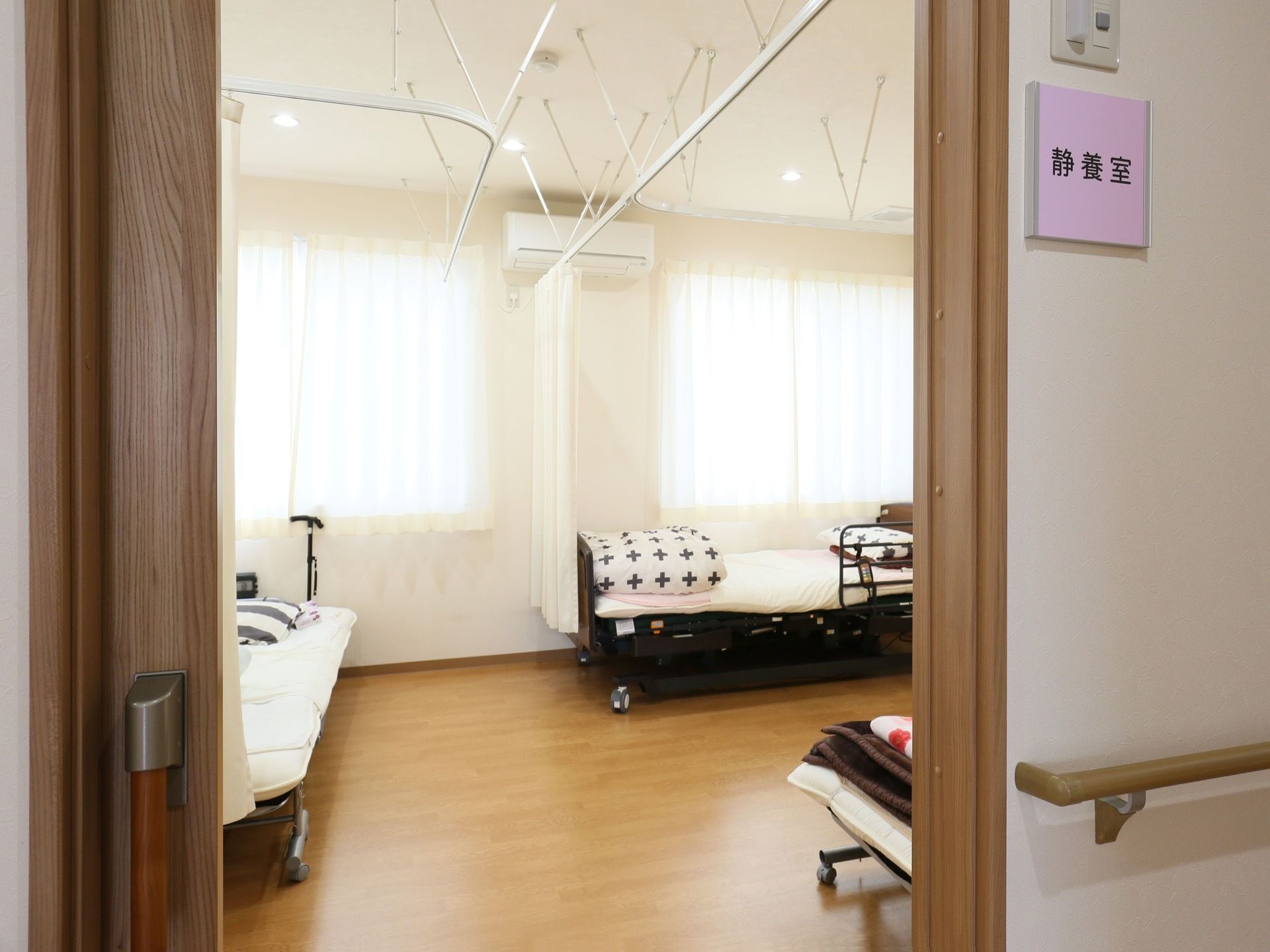 ドアから静養室を覗いた様子。ベッドが複数置かれ、それぞれに毛布やまくらが準備されている。上部にはエアコンが取り付けられている。