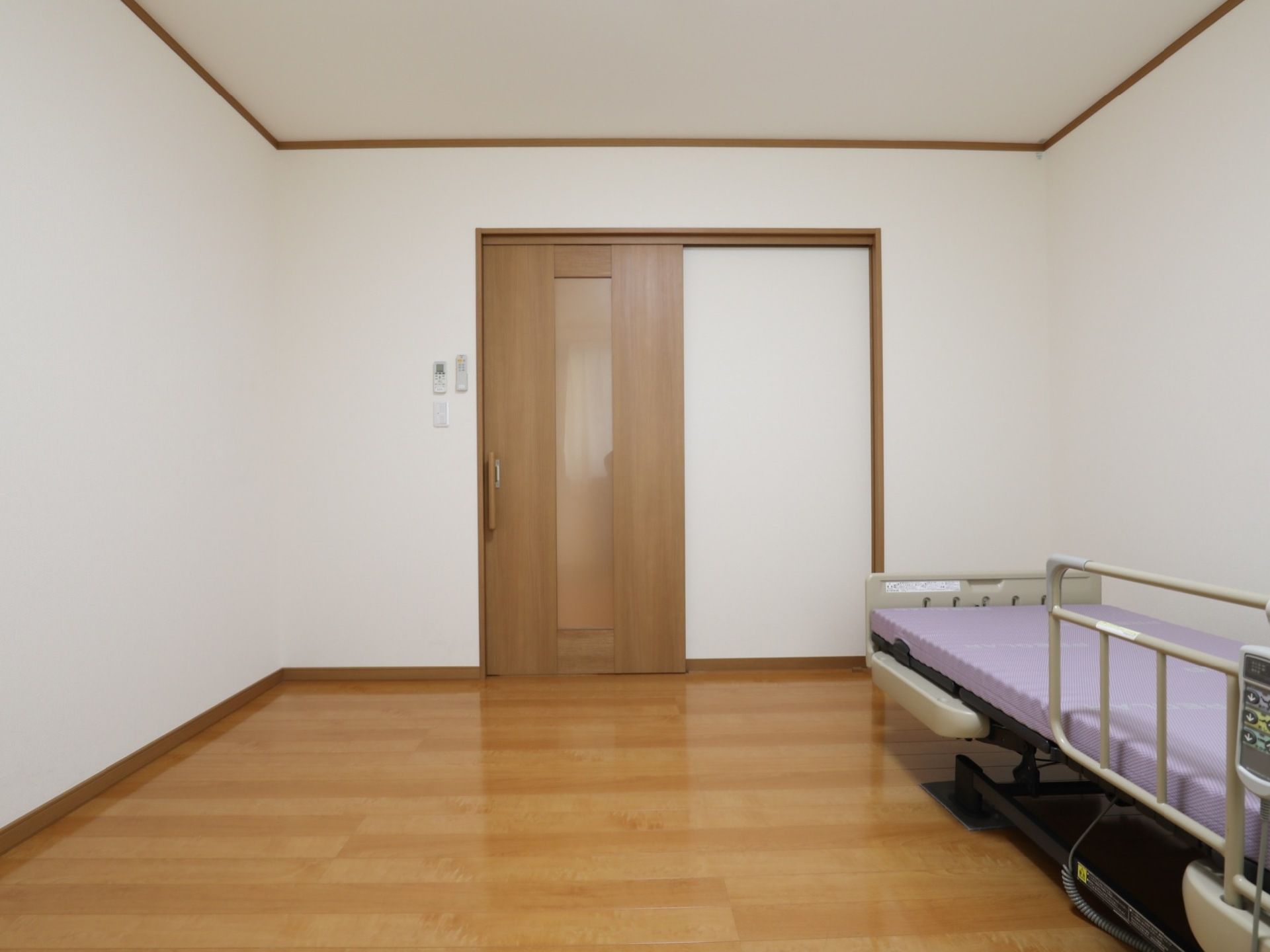 居室の扉は、木製の引き戸となっている。入口横の壁には、照明とエアコンのリモコンが取りつけられている。