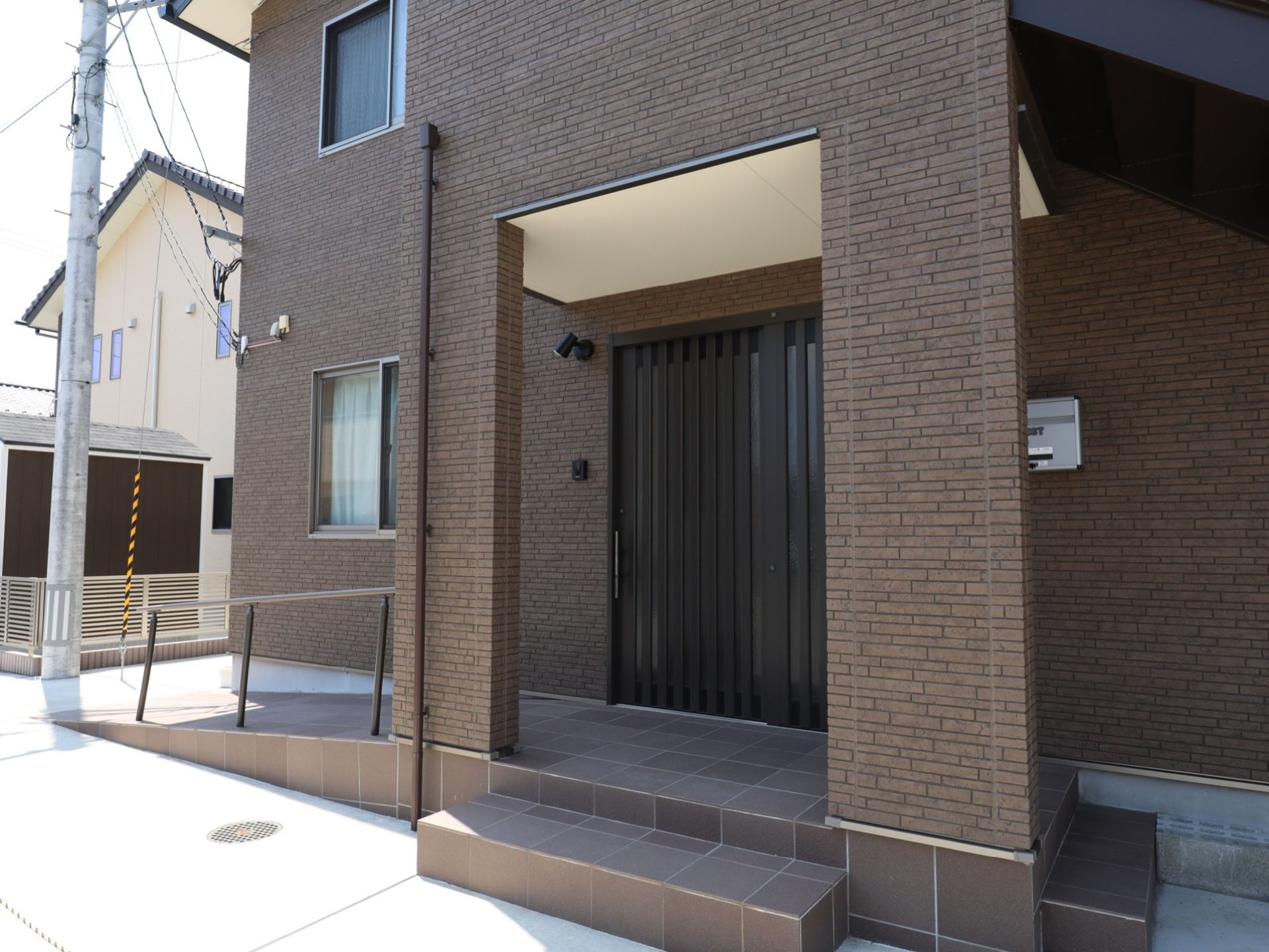 住宅街の中にあるグループホーム。２階建ての建物で、まるで一軒家のような外観である。玄関には照明が設置されている。