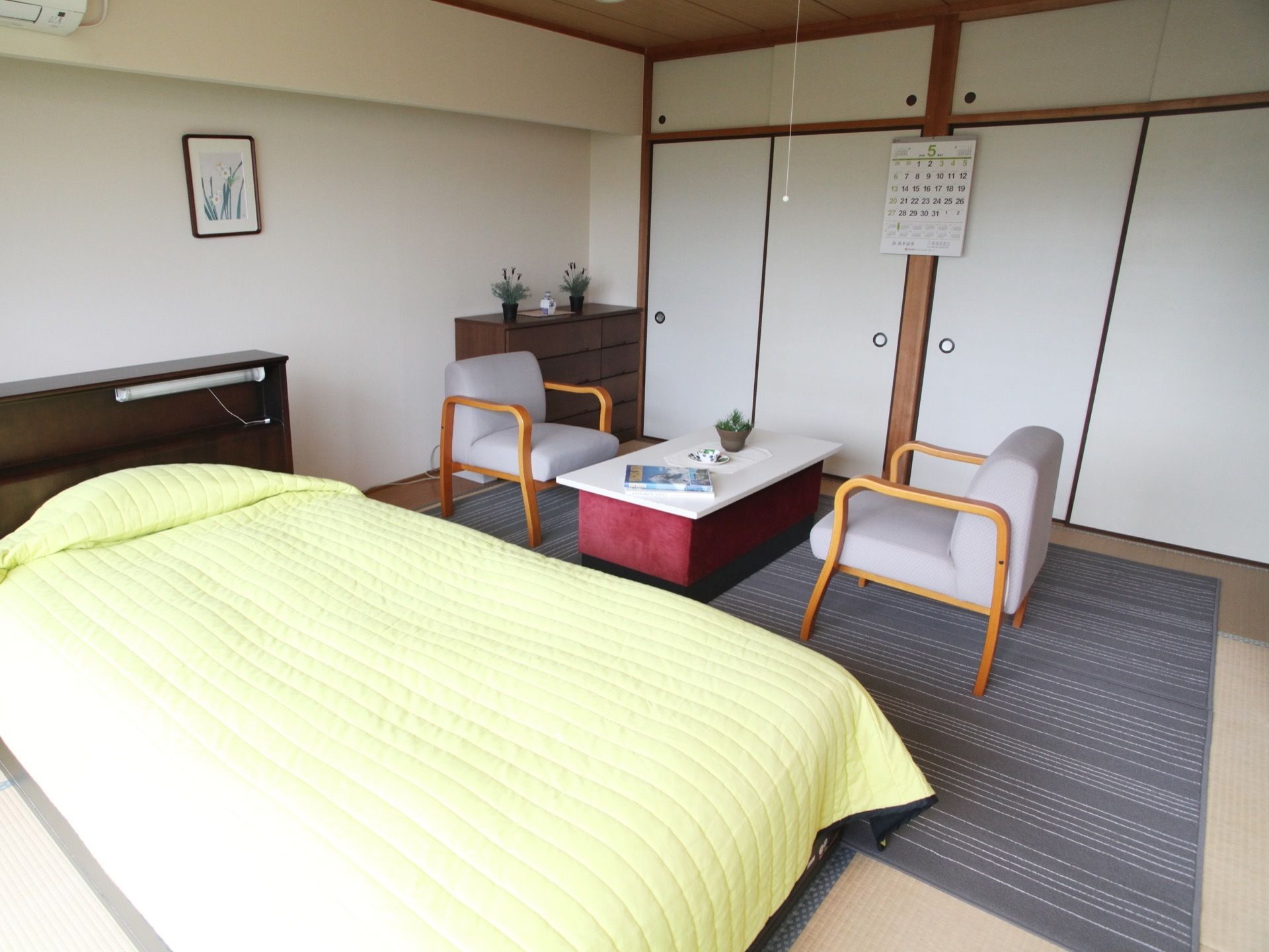 ベッドと応接セットが置かれている居室。落ち着いた色合いのカーペットが敷かれている。小さな観葉植物がある。
