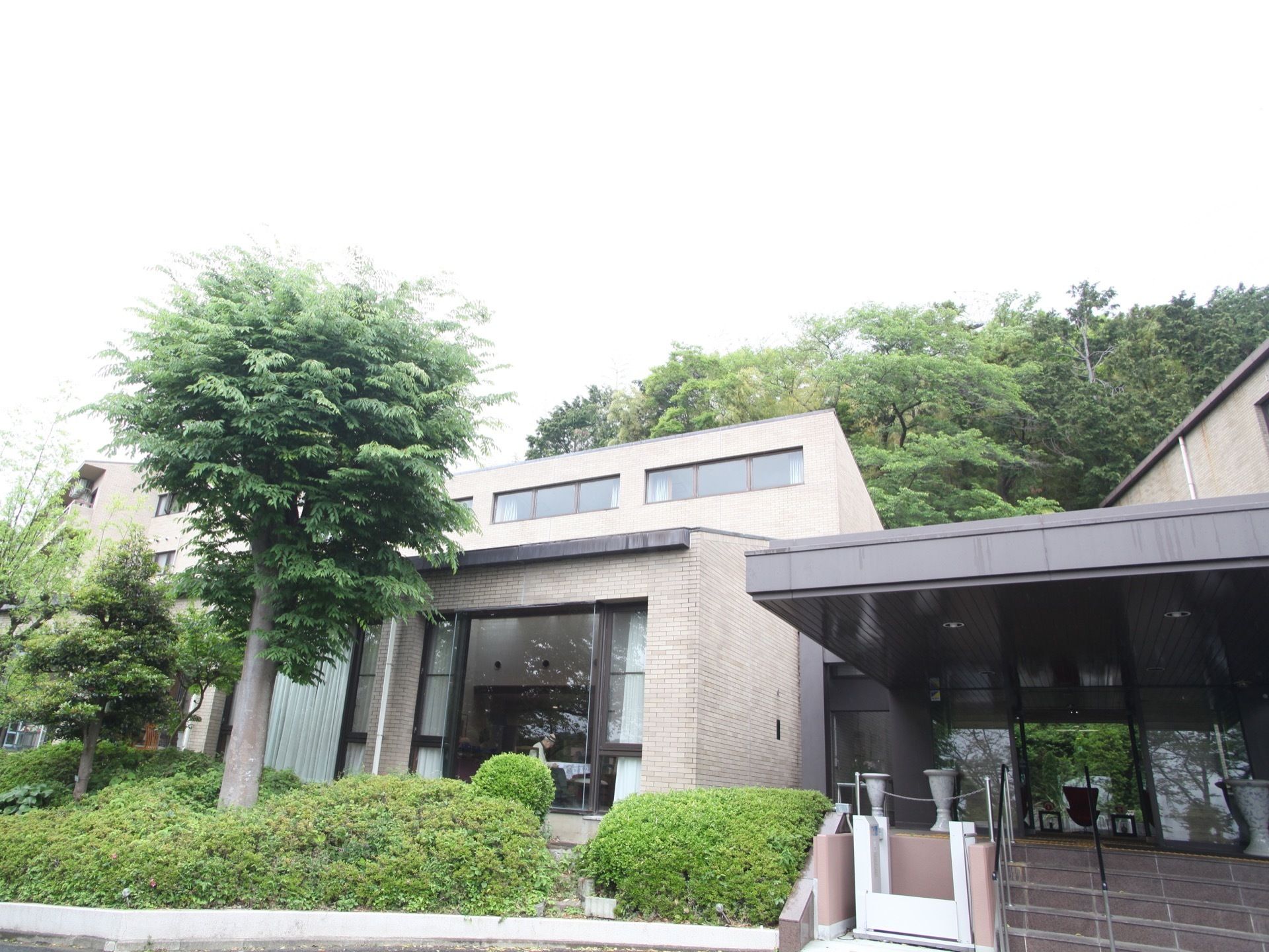 レンガ調のきれいな外観。緑がよく見える大きいガラス窓がある。玄関前の階段には体の幅より少し広い手すりがある。