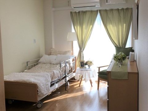 床がフローリングで、壁や天井が白色の広々とした空間である。介護ベッドが置いてある。エアコンが設置されている。