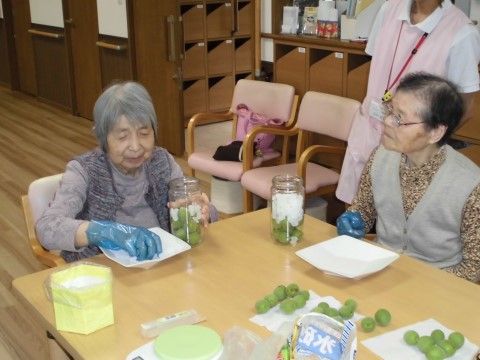 椅子に座り手袋をして緑色のだんごを作っている、女性入居者様