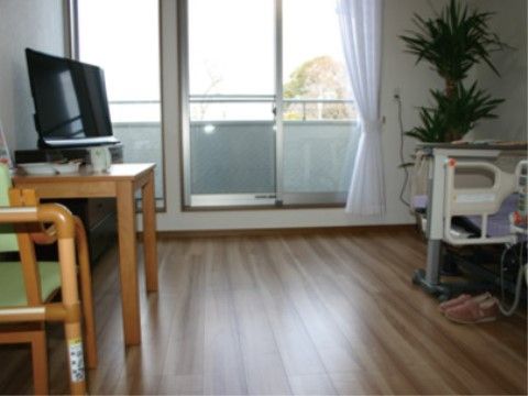 床がフローリングの居室である。介護ベッドや椅子が置かれている。テーブルの上には、テレビが設置されている。