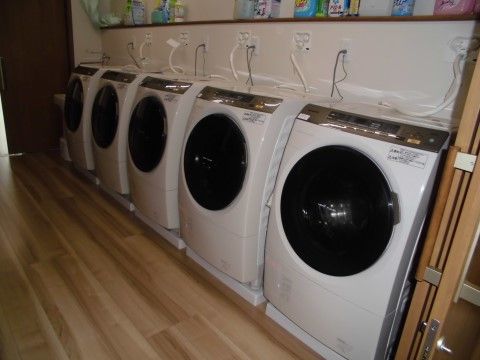 ５台のドラム式洗濯乾燥機を備えた広い洗濯室である。用途に合わせて選べるよう、数種類の洗濯洗剤が置かれている。
