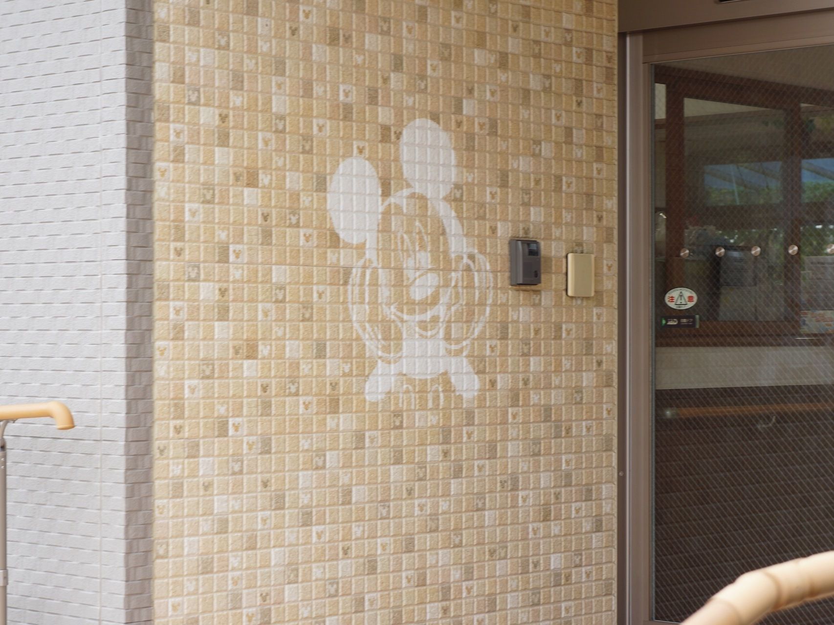 正面玄関の入口の壁に、人気キャラクターの絵が描かれている。小さなタイルにもキャラクターのモチーフがある。壁にはインターホンが設置されている。