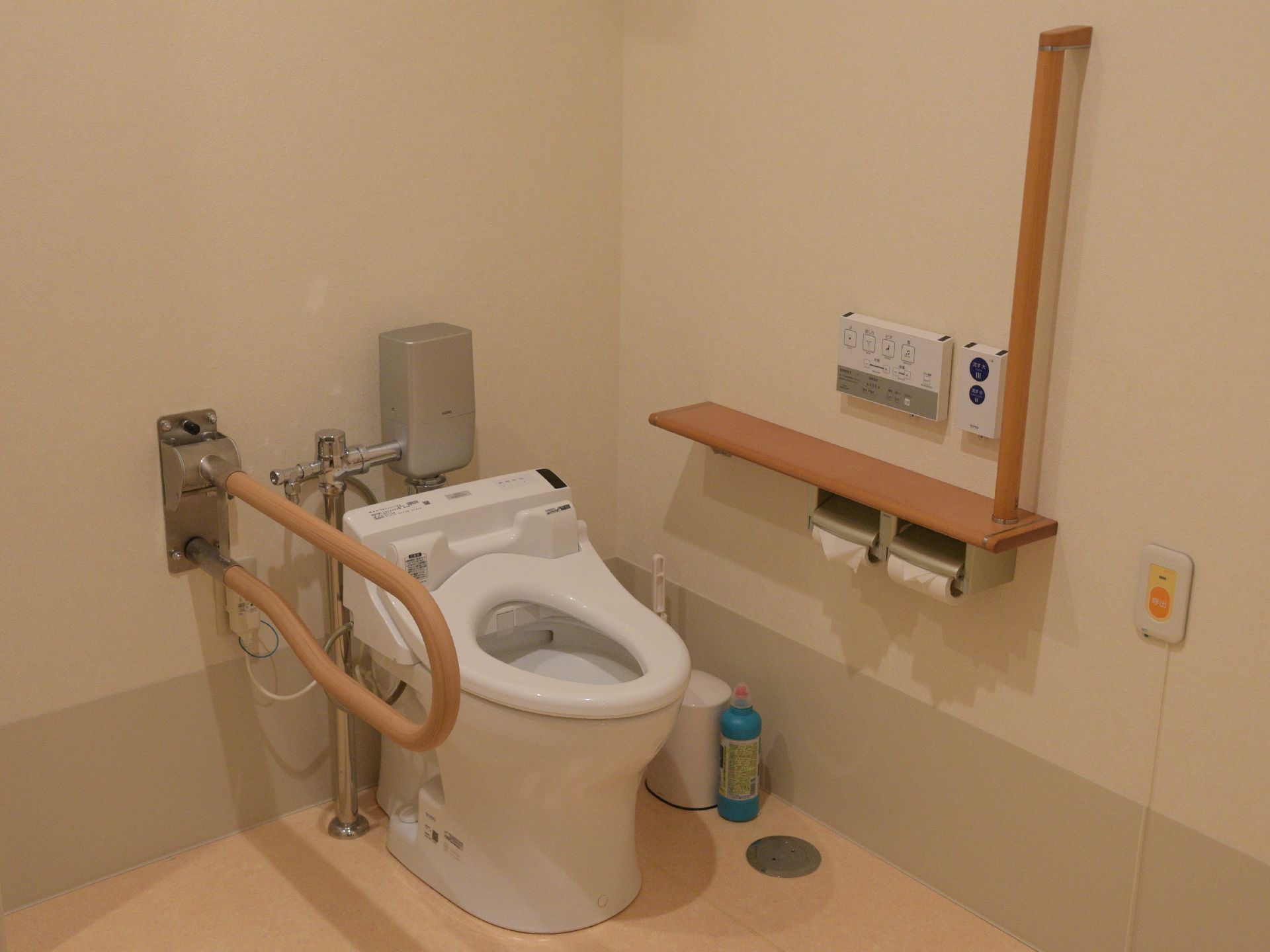 トイレの内装はアイボリー系が基調である。ウッド調の手すりが両側にあり、小さな棚もある。ウォシュレットのボタンやナースコールもついている。